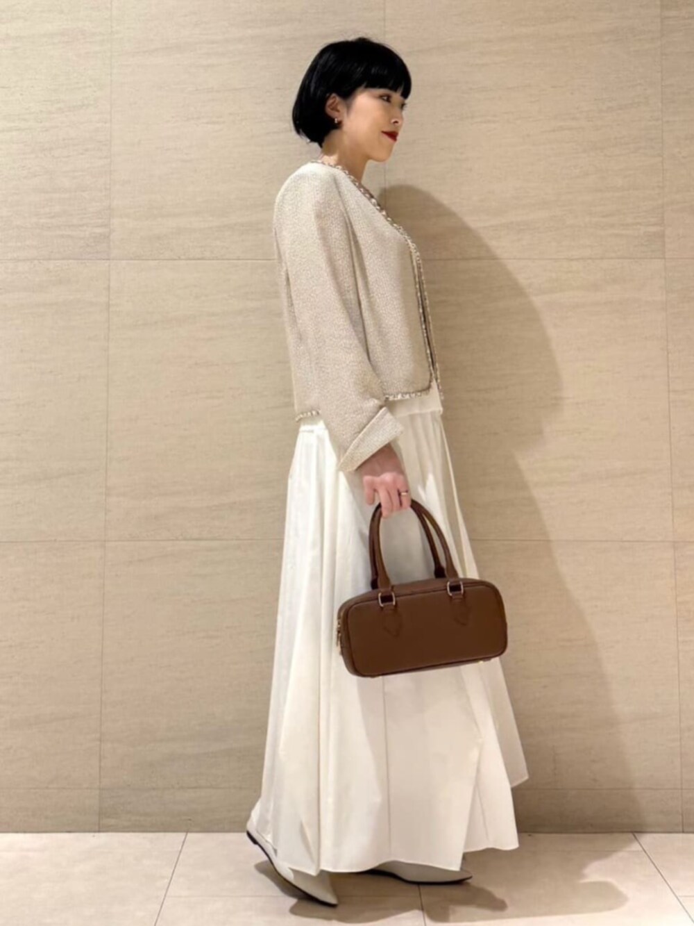 ホワイト系のパンプス、ブラウン系のボストンバッグ、ゴールド系のネックレスを着用したレディースの春コーディネートの4枚目の写真