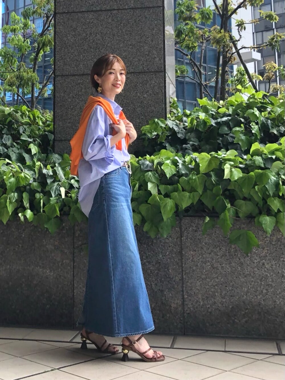 オレンジ系のニット/セーター、ブルー系のシャツ/ブラウス、ブルー系のスカートを着用したレディースの春コーディネートの2枚目の写真