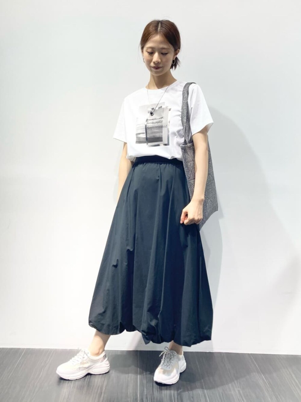 ブラック系のスカート、グレー系のトートバッグ、ホワイト系のTシャツ/カットソーを着用したレディースの夏コーディネートの2枚目の写真