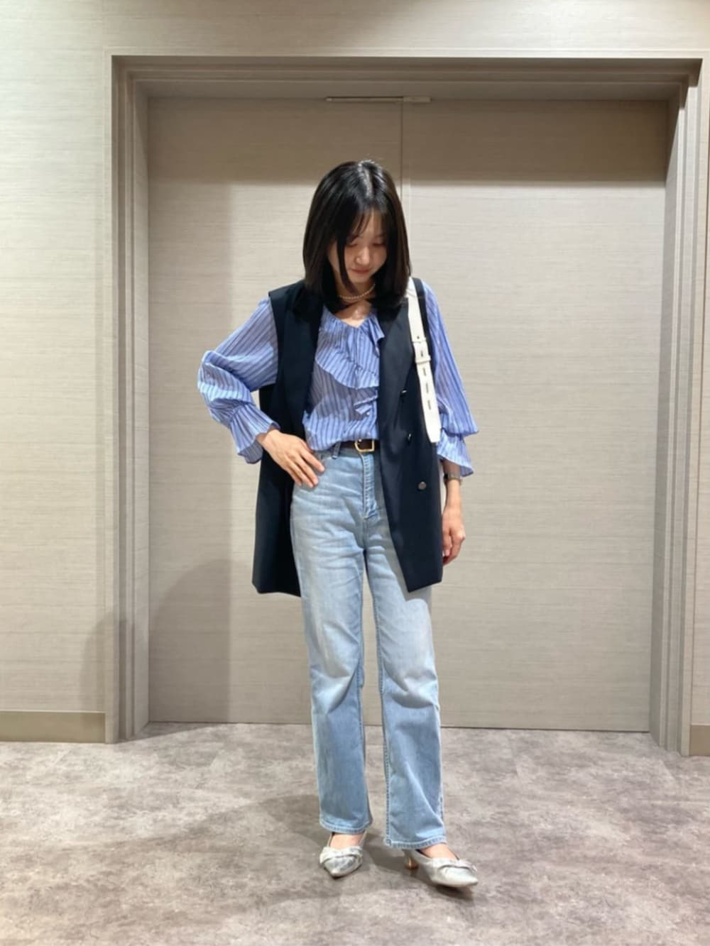 ホワイト系のショルダーバッグ、ブルー系のシャツ/ブラウス、ブラック系のベストを着用したレディースの春コーディネートの2枚目の写真