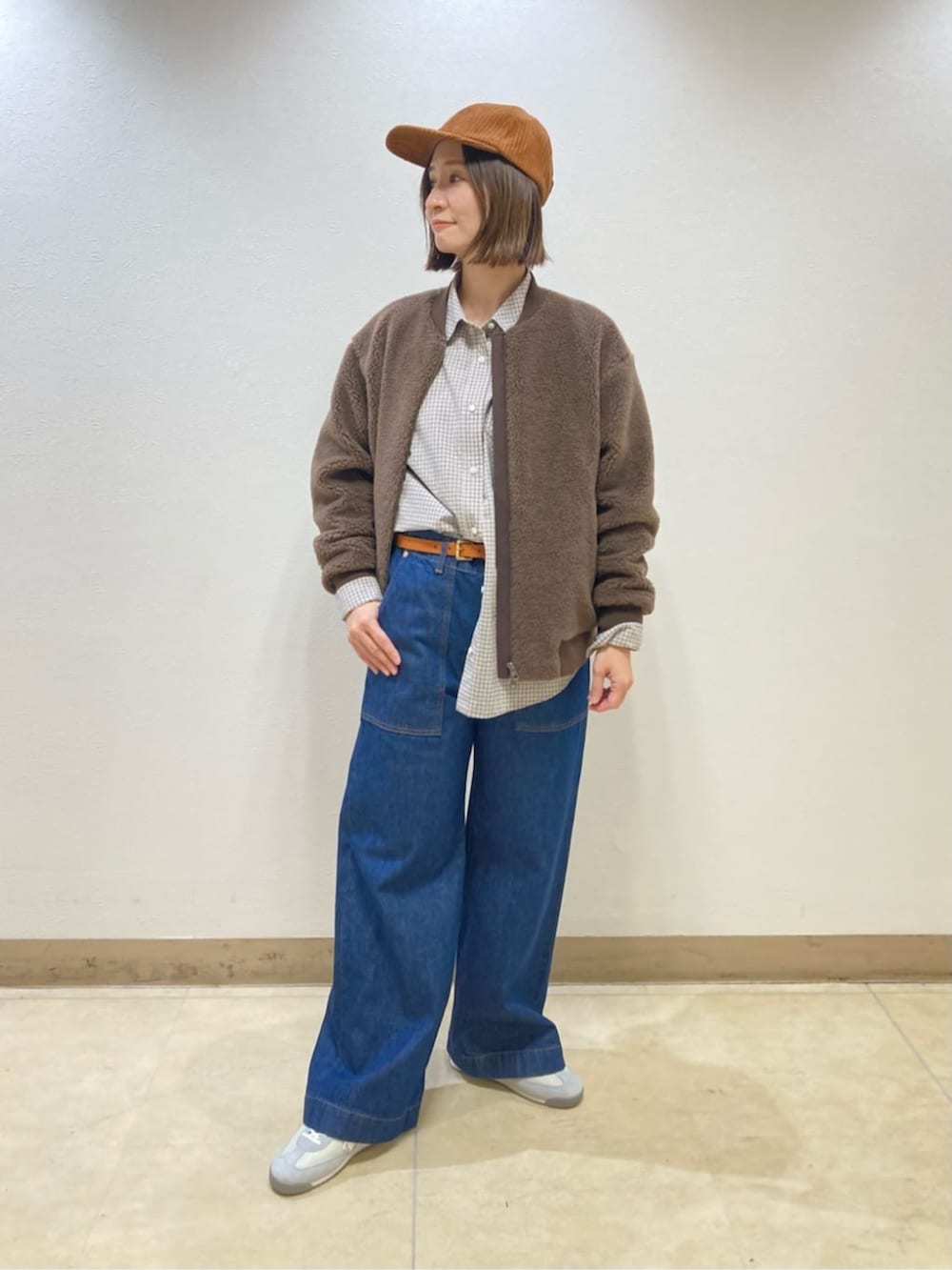 ブラウン系のブルゾン、ブルー系のデニムパンツ、イエロー系のキャップを着用したレディースの秋コーディネートの2枚目の写真