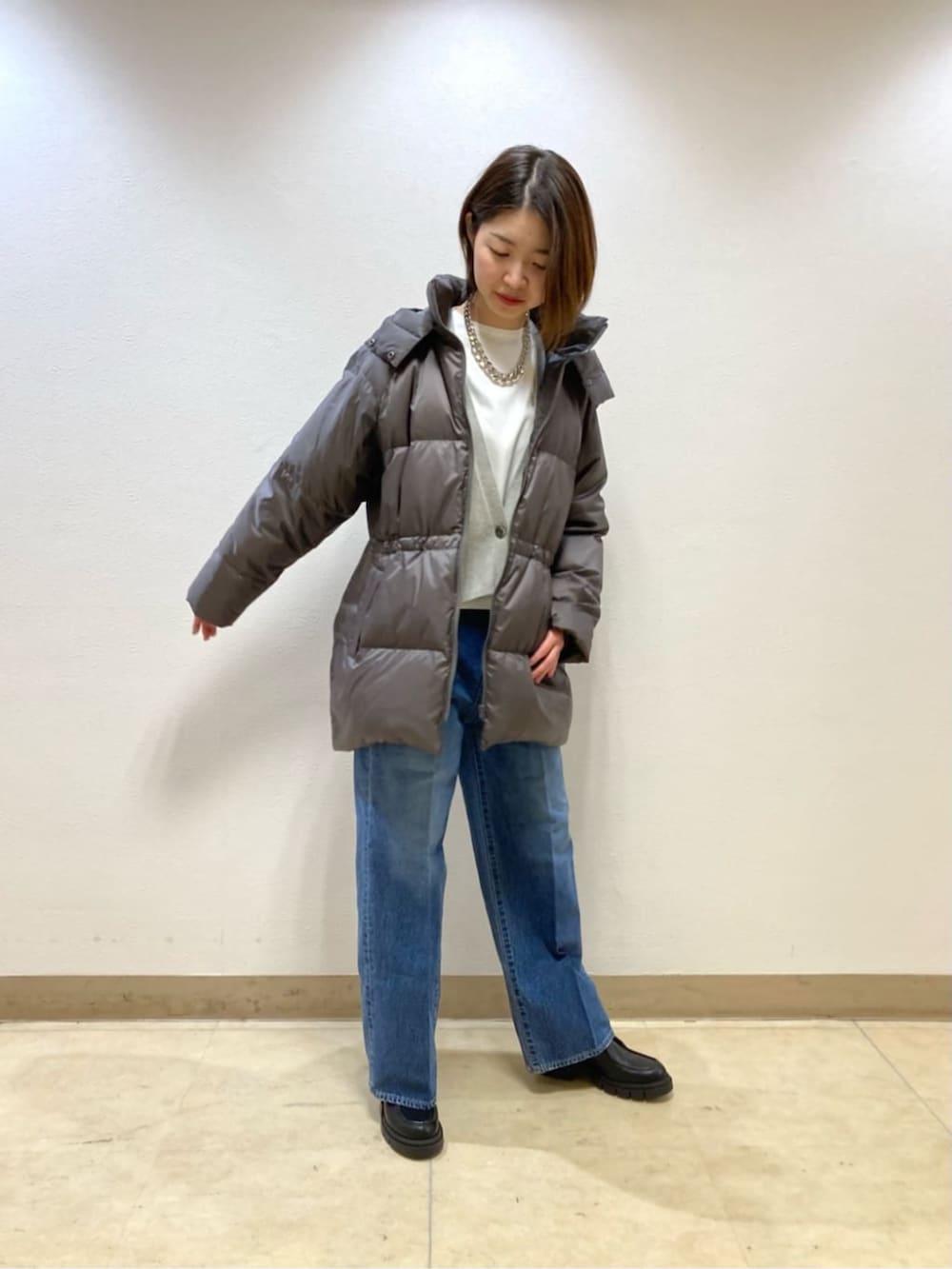 ブルー系のデニムパンツ、グレー系のダウンジャケット/コート、ベージュ系のカーディガン/ボレロを着用したレディースの冬コーディネートの2枚目の写真