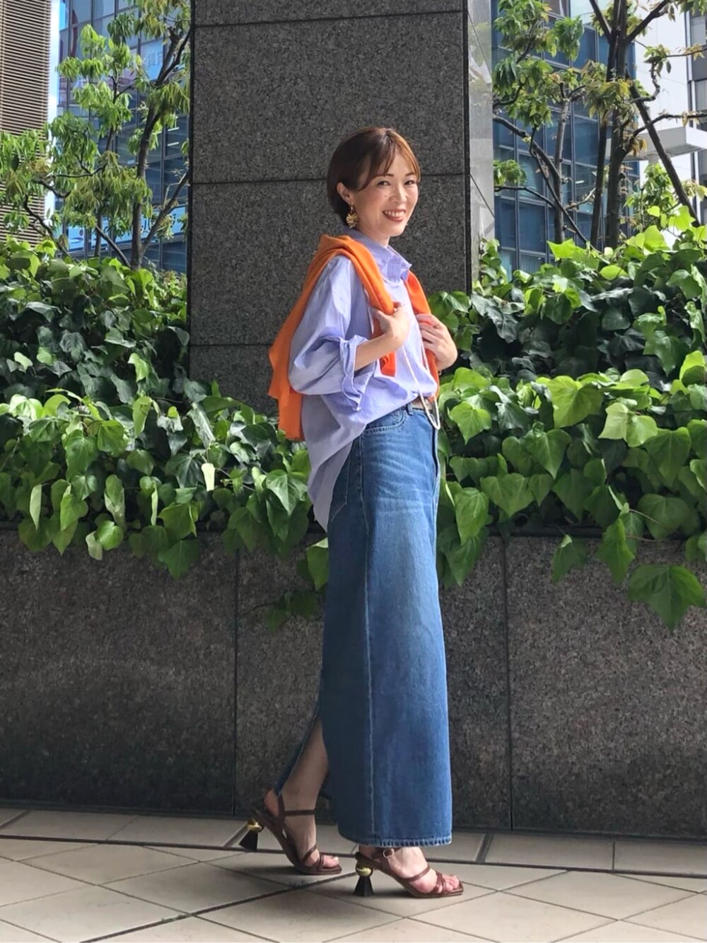 オレンジ系のニット/セーター、ブルー系のシャツ/ブラウス、ブルー系のスカートを着用したレディースの春コーディネートの3枚目の写真