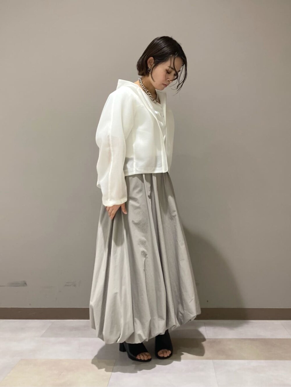 ベージュ系のスカート、ホワイト系のTシャツ/カットソー、ブラック系のサンダルを着用したレディースの春コーディネートの2枚目の写真