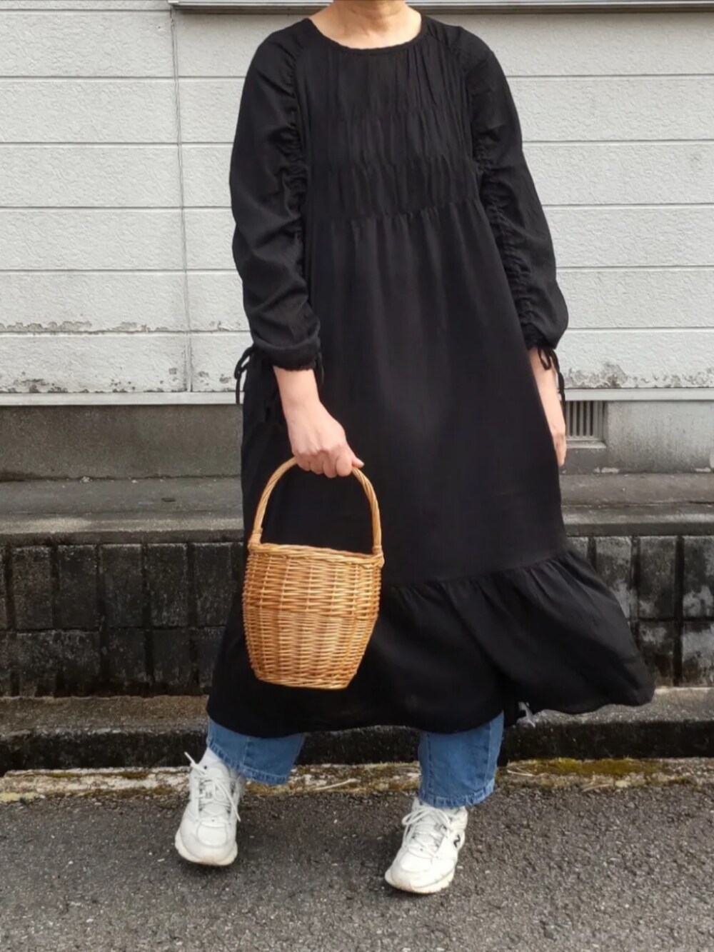 ブラック系のワンピース、ベージュ系のかごバッグ、ホワイト系のスニーカーを着用したレディースの春コーディネートの2枚目の写真