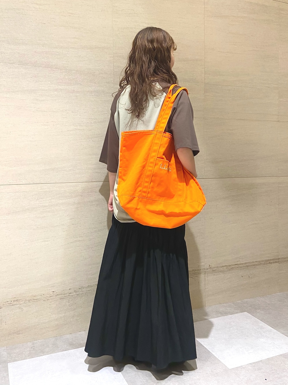 ブラック系のスカート、オレンジ系のトートバッグ、ブラウン系のTシャツ/カットソーを着用したレディースの夏コーディネートの2枚目の写真