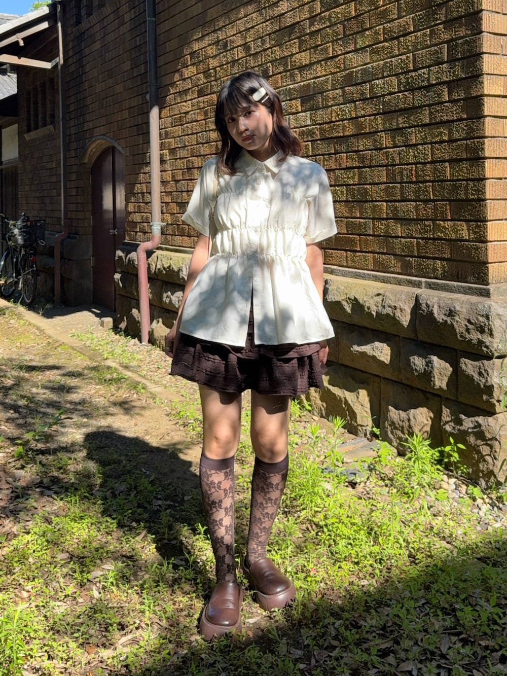 ブラウン系のスカート、ブラック系のサンダル、ベージュ系のシャツ/ブラウスを着用したレディースの夏コーディネートの2枚目の写真