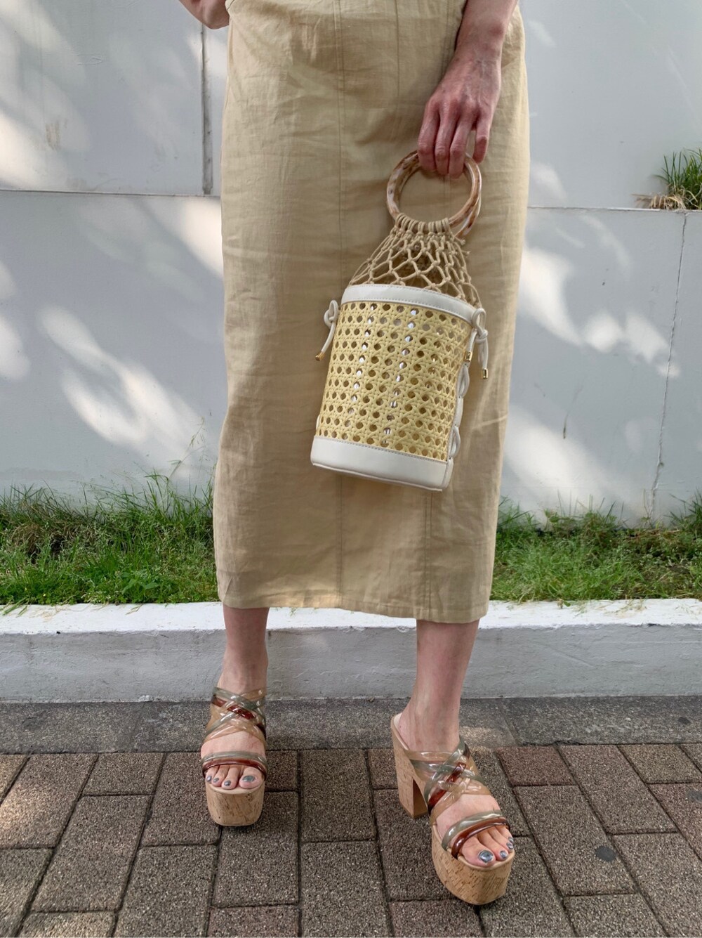 ホワイト系のハンドバッグ、イエロー系のワンピース、ゴールド系のピアス（両耳用）を着用したレディースの夏コーディネートの5枚目の写真