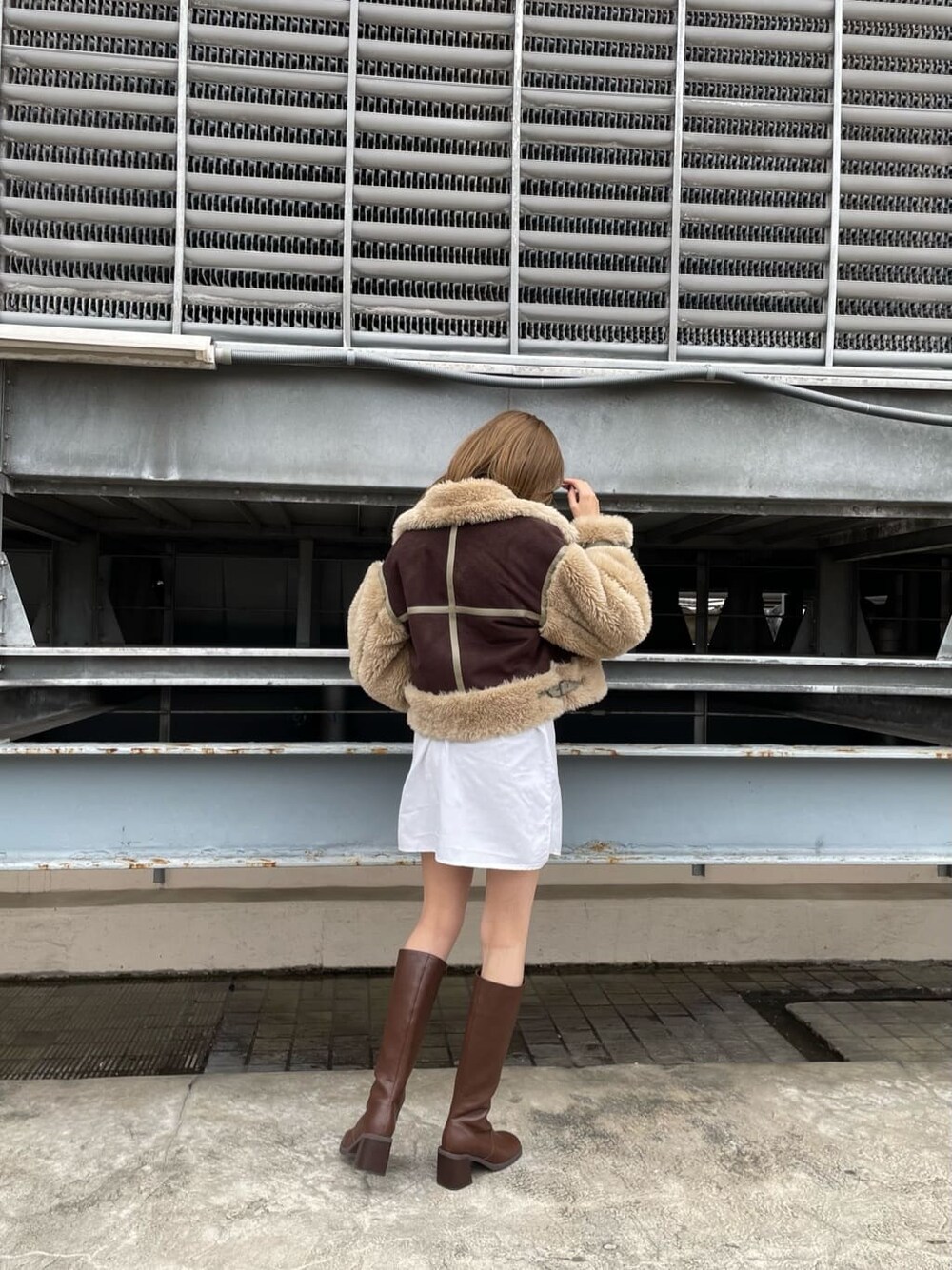 ブラウン系のムートンコート、ブラック系のハンドバッグ、ブラウン系のブーツを着用したレディースの秋コーディネートの3枚目の写真