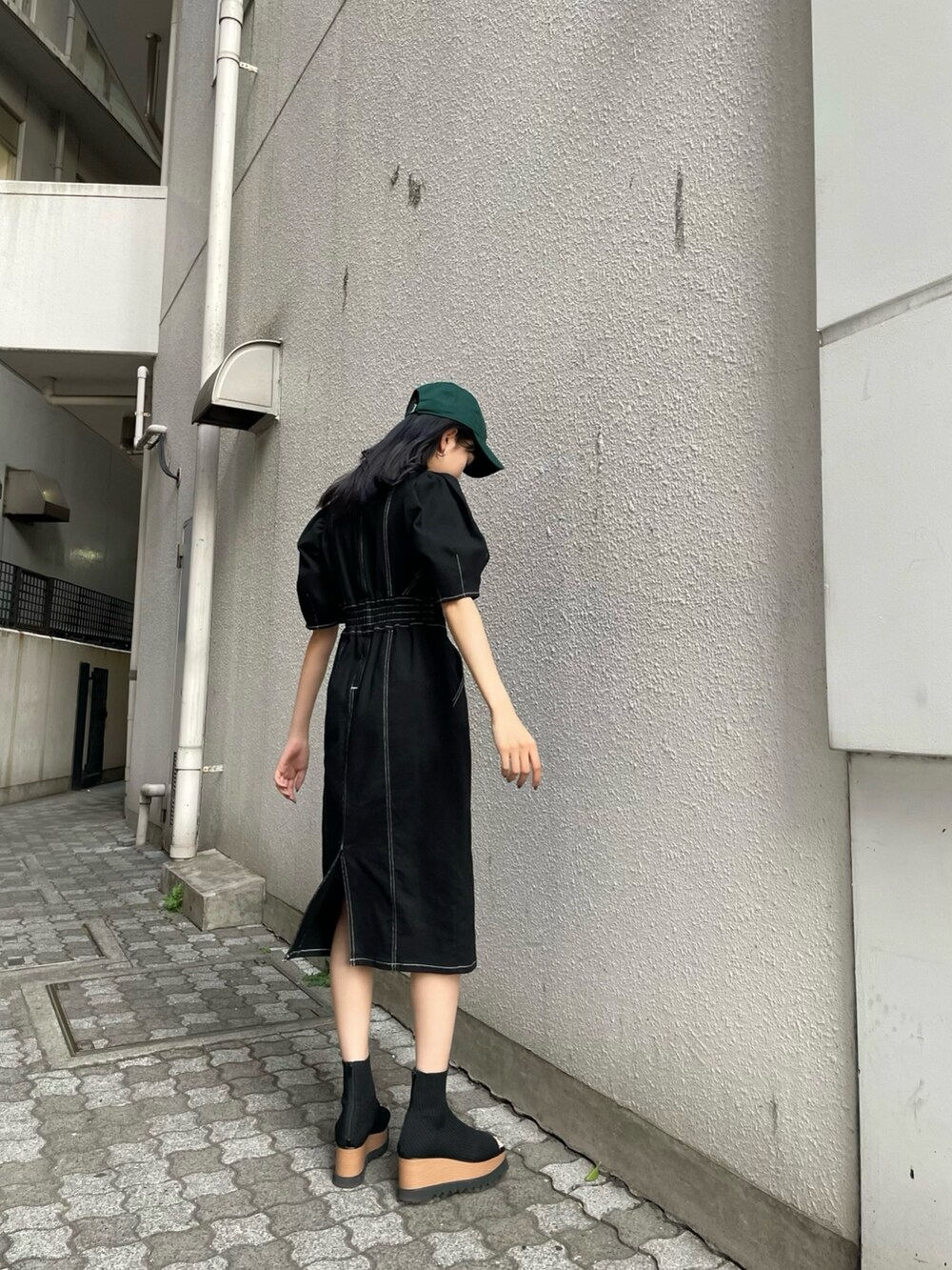 ブラック系のワンピース、ブラック系のブーツ、グリーン系のキャップを着用したレディースの春コーディネートの2枚目の写真