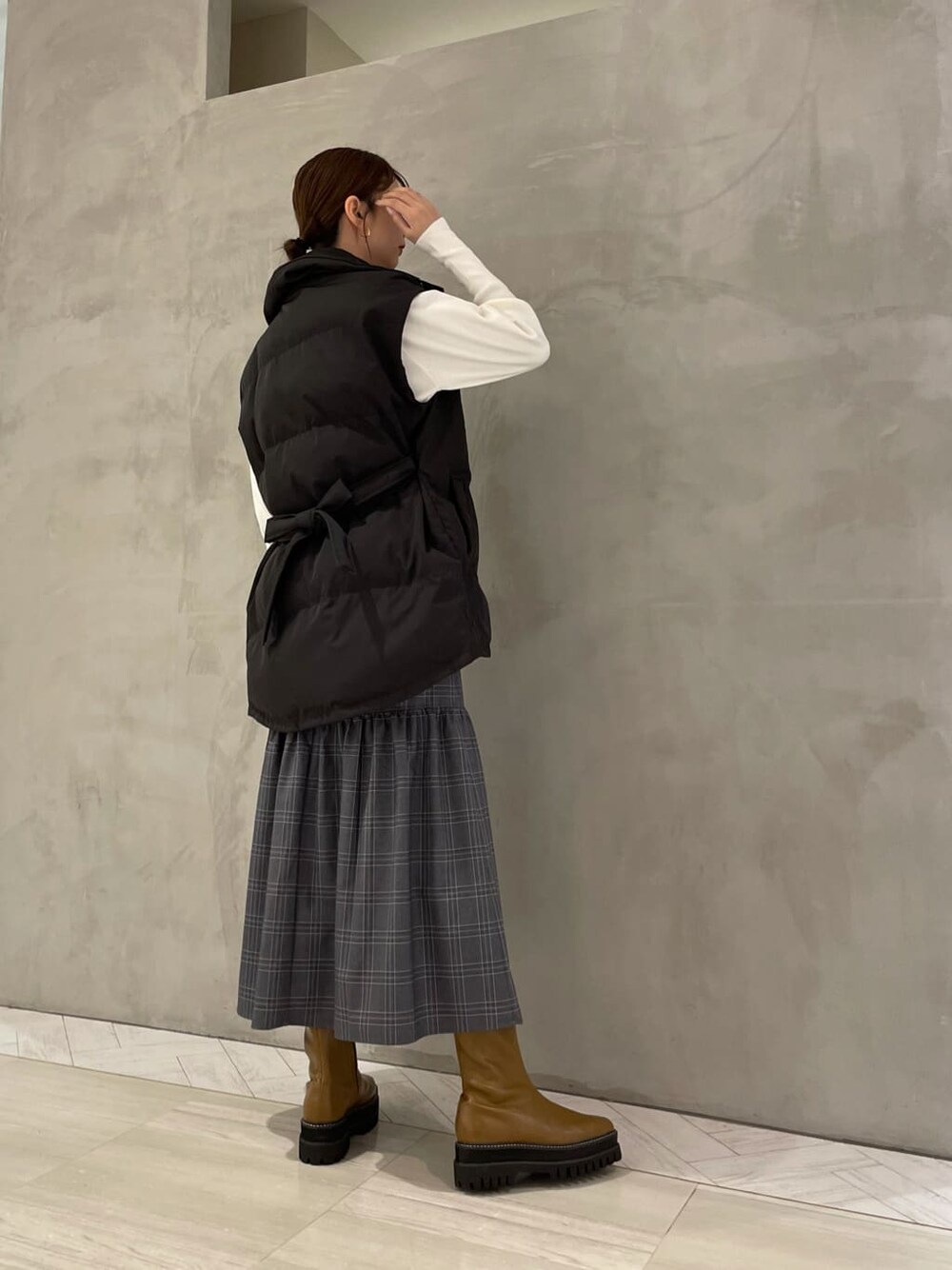 ブラック系のダウンベスト、その他のスカート、ブラウン系のブーツを着用したレディースの秋コーディネートの2枚目の写真