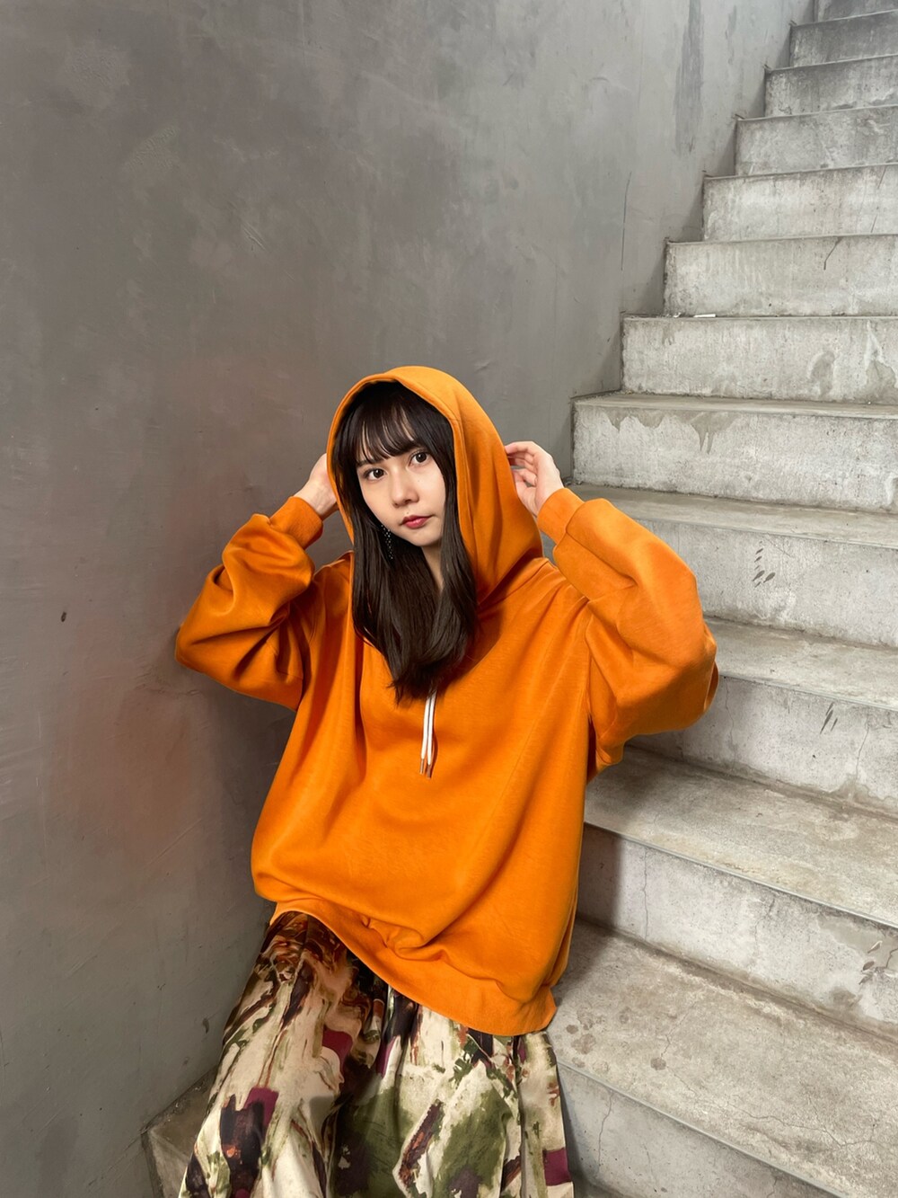 オレンジ系のパーカー、グリーン系のスカート、ホワイト系のブーツを着用したレディースの夏コーディネートの6枚目の写真