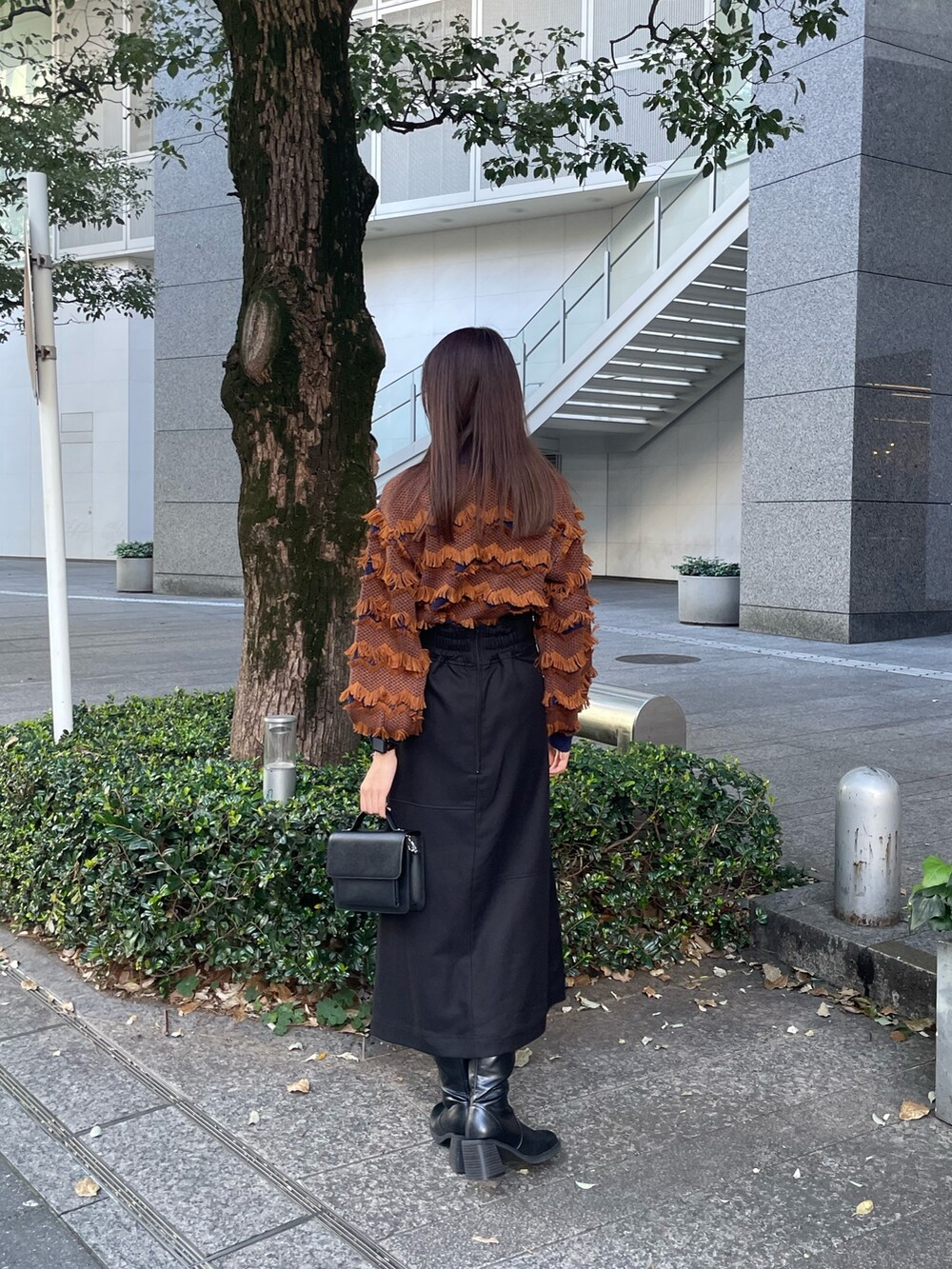 オレンジ系のニット/セーター、ブラック系のスカート、ブラック系のブーツを着用したレディースの秋コーディネートの4枚目の写真