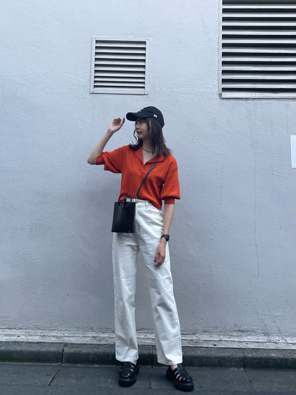 オレンジ系のポロシャツ、ホワイト系のデニムパンツ、ブラック系のサンダルを着用したレディースの夏コーディネートの2枚目の写真