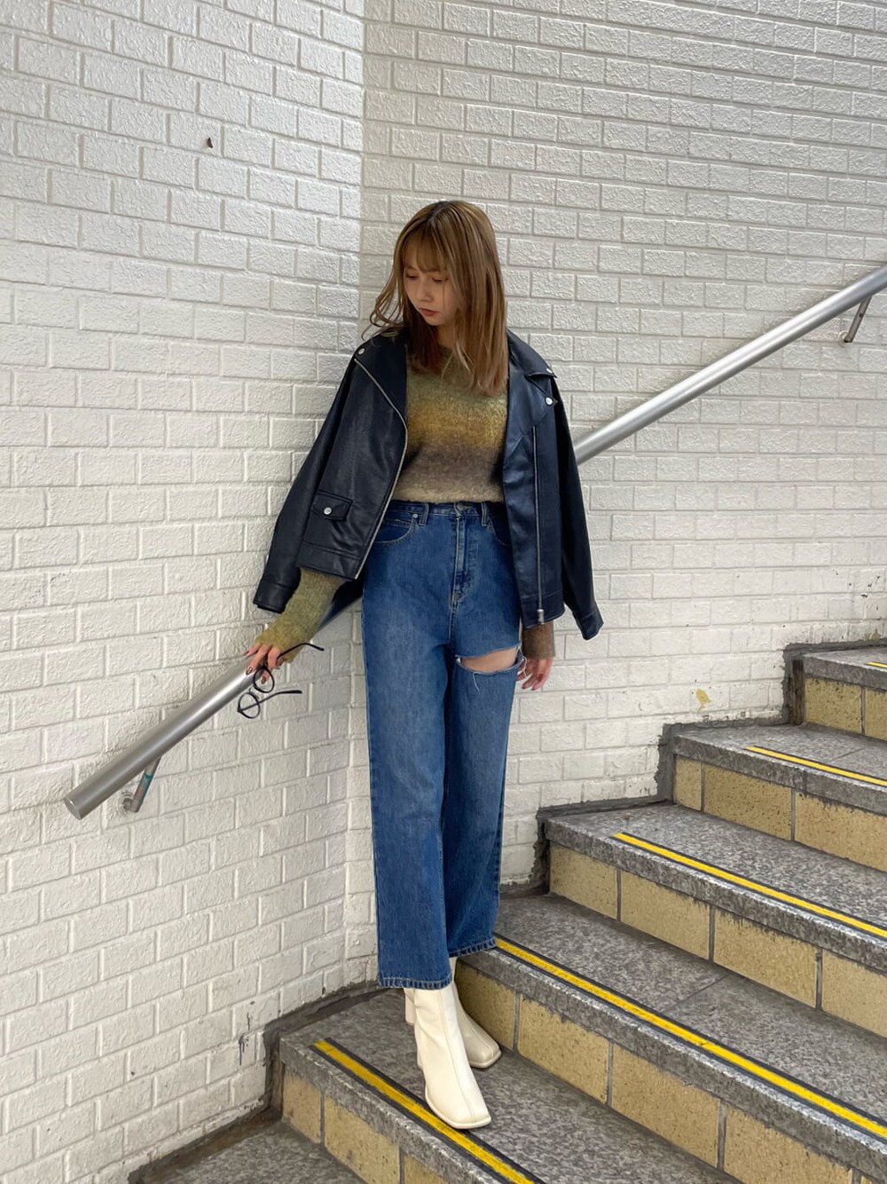 ブラック系のライダースジャケット、ホワイト系のブーツ、ブルー系のデニムパンツを着用したレディースの秋コーディネートの3枚目の写真