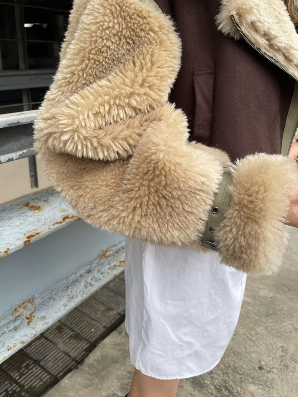 ブラウン系のムートンコート、ブラック系のハンドバッグ、ブラウン系のブーツを着用したレディースの秋コーディネートの4枚目の写真