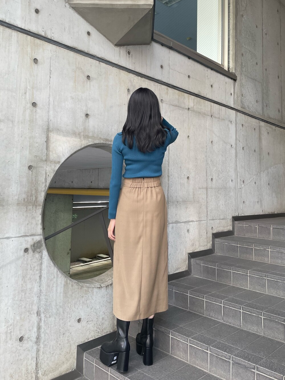 ブルー系のニット/セーター、ベージュ系のスカート、ブラック系のブーツを着用したレディースの夏コーディネートの3枚目の写真