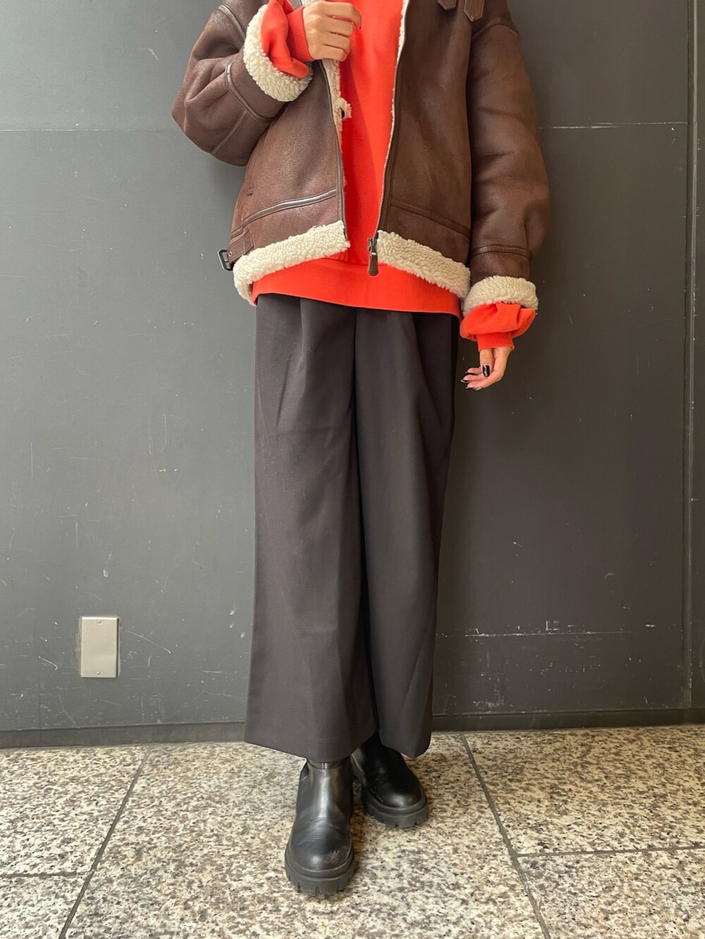 オレンジ系のパーカー、ブラウン系のムートンコート、ブラック系のスラックスを着用したレディースの秋コーディネートの8枚目の写真
