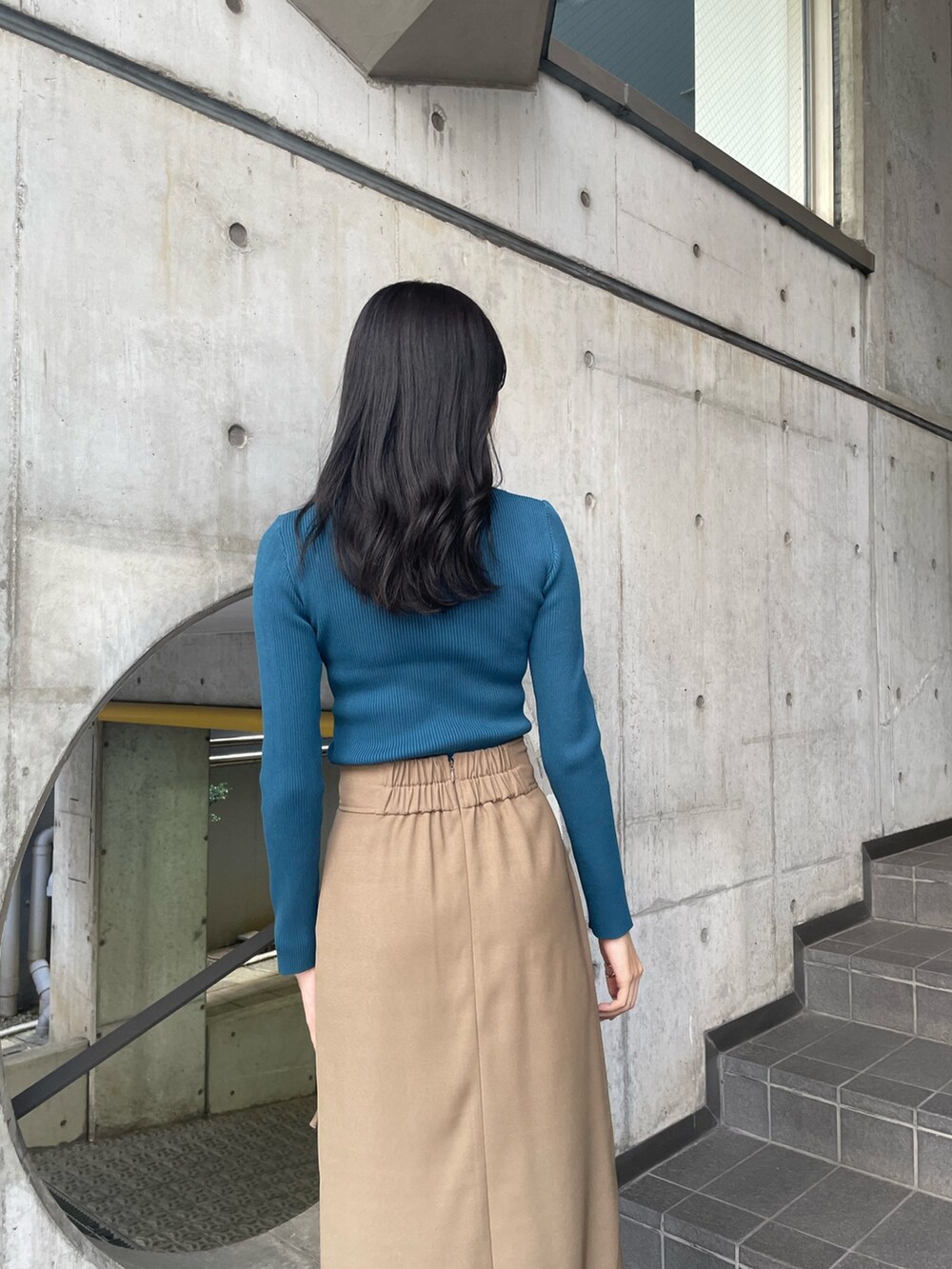 ブルー系のニット/セーター、ベージュ系のスカート、ブラック系のブーツを着用したレディースの夏コーディネートの5枚目の写真