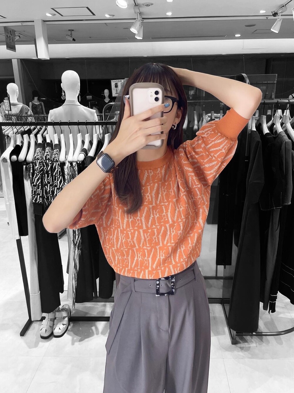 オレンジ系のニット/セーター、グレー系のスラックスを着用したレディースの夏コーディネートの2枚目の写真