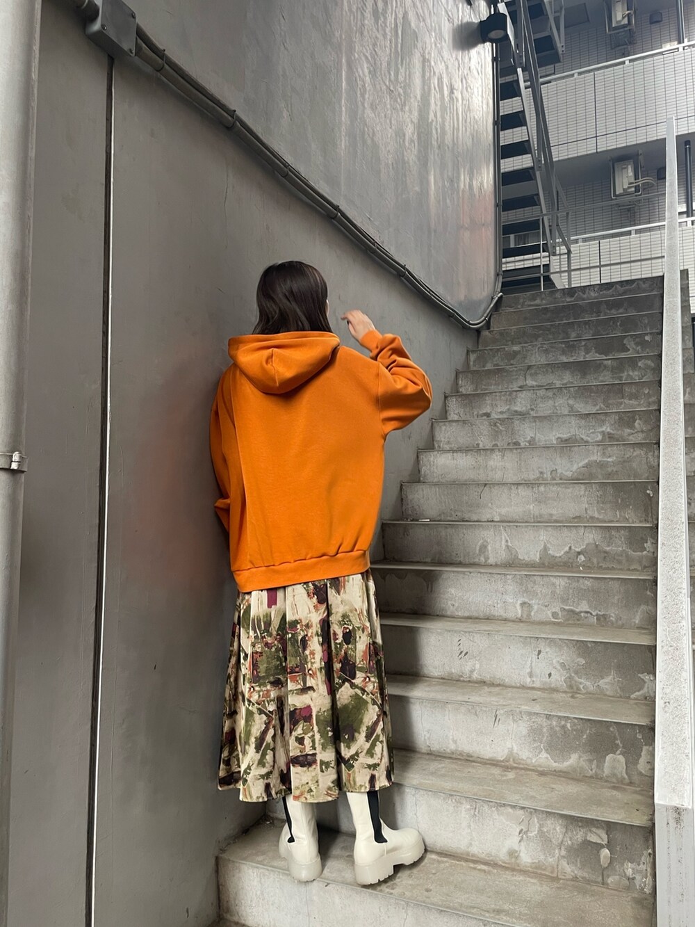 オレンジ系のパーカー、グリーン系のスカート、ホワイト系のブーツを着用したレディースの夏コーディネートの3枚目の写真