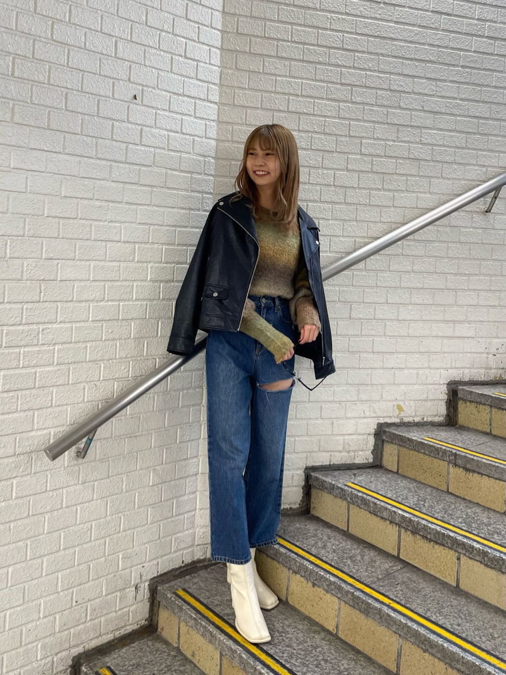 ブラック系のライダースジャケット、ホワイト系のブーツ、ブルー系のデニムパンツを着用したレディースの秋コーディネートの2枚目の写真