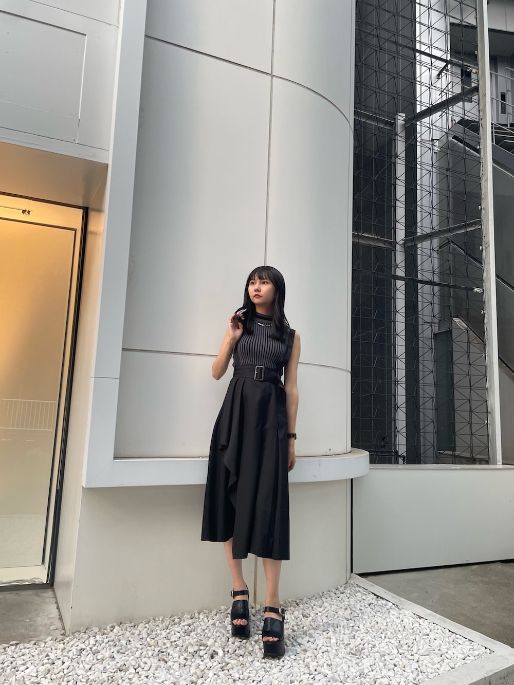 ブラック系のニット/セーター、ブラック系のジャンパースカート、ブラック系のサンダルを着用したレディースの春コーディネートの3枚目の写真