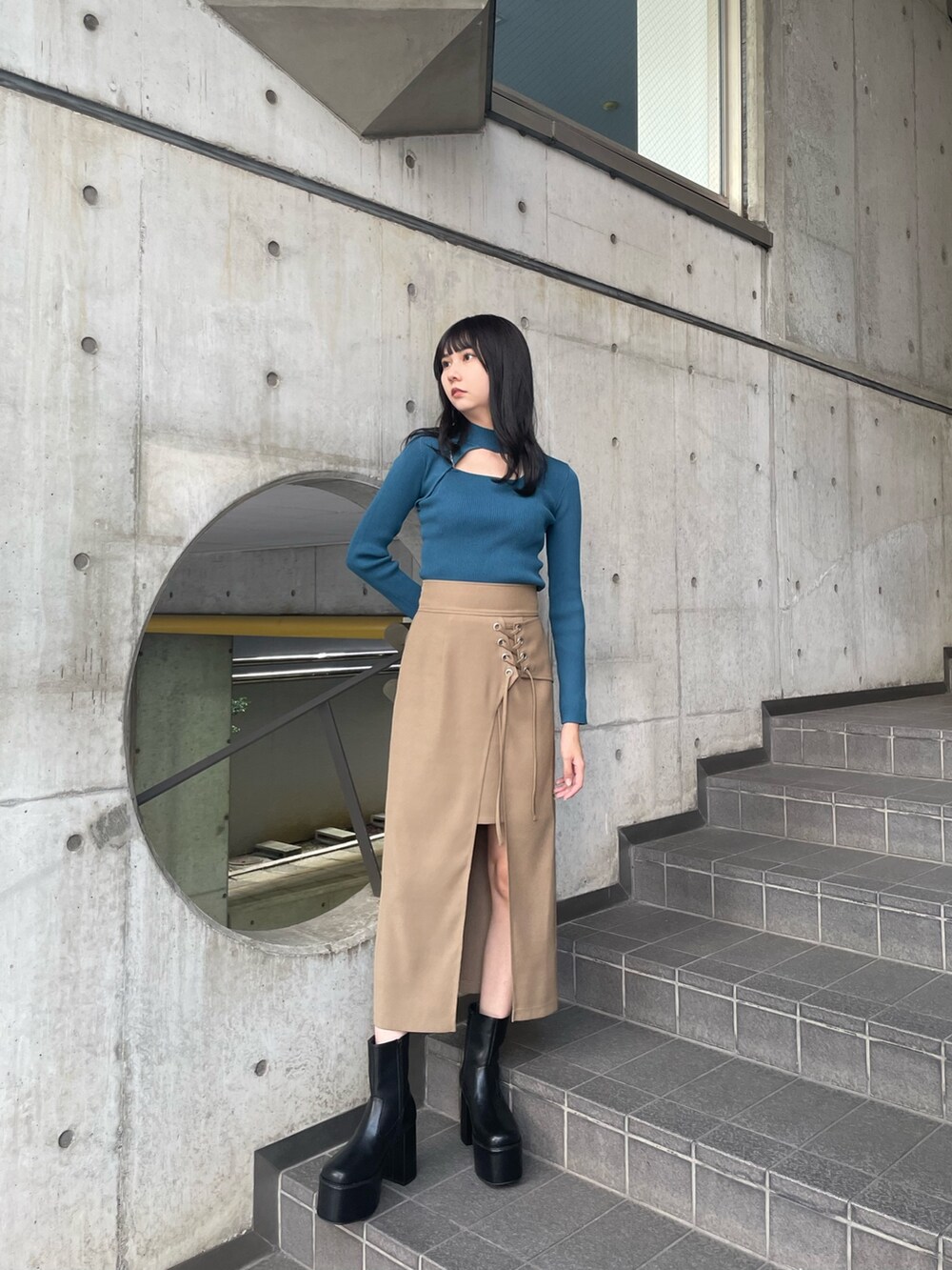 ブルー系のニット/セーター、ベージュ系のスカート、ブラック系のブーツを着用したレディースの夏コーディネートの2枚目の写真