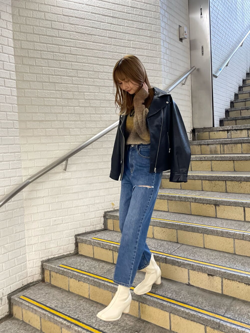 ブラック系のライダースジャケット、ホワイト系のブーツ、ブルー系のデニムパンツを着用したレディースの秋コーディネートの4枚目の写真