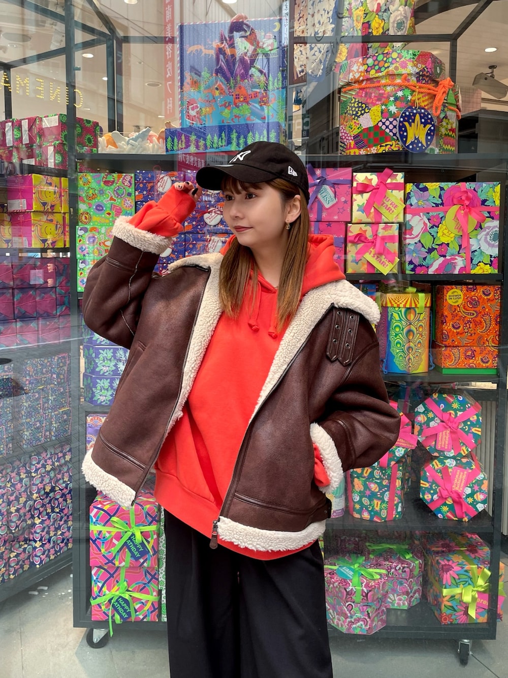 オレンジ系のパーカー、ブラウン系のムートンコート、ブラック系のスラックスを着用したレディースの秋コーディネートの3枚目の写真