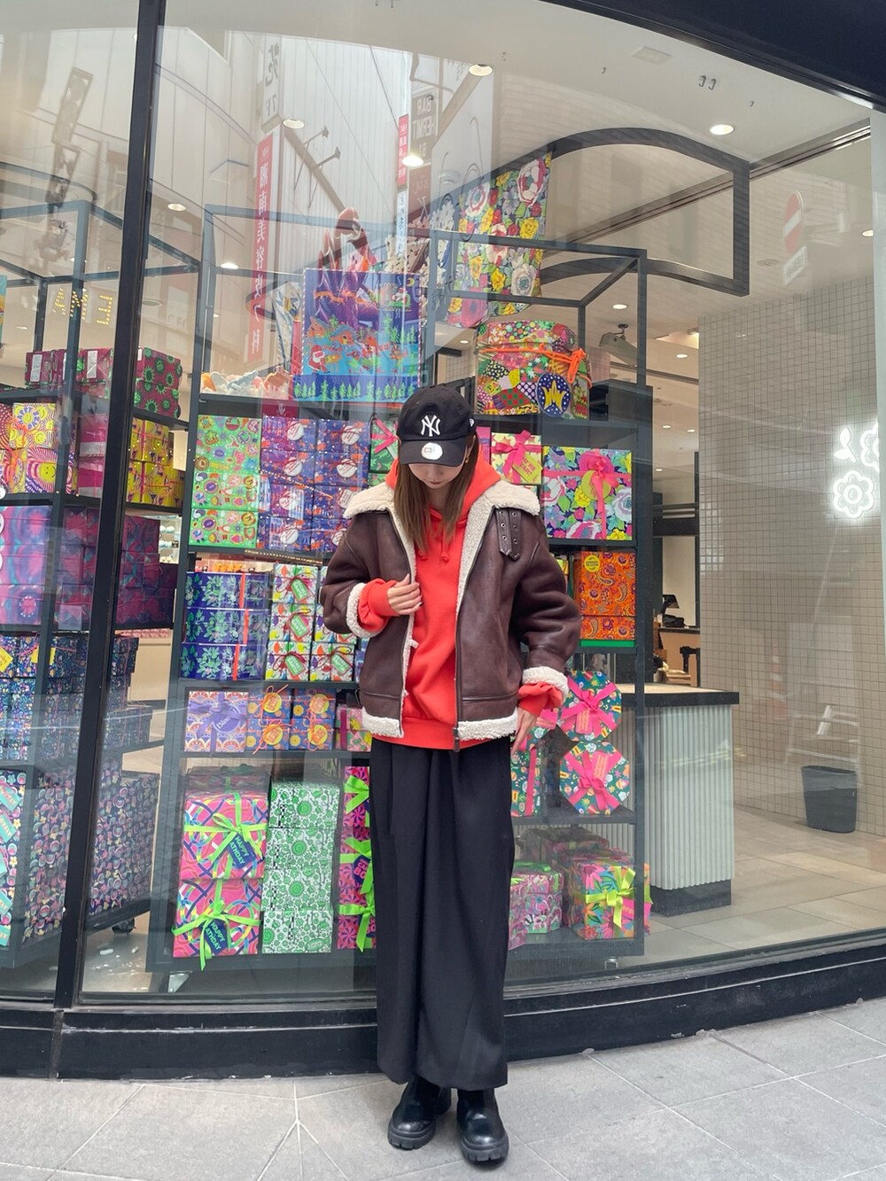 オレンジ系のパーカー、ブラウン系のムートンコート、ブラック系のスラックスを着用したレディースの秋コーディネートの2枚目の写真