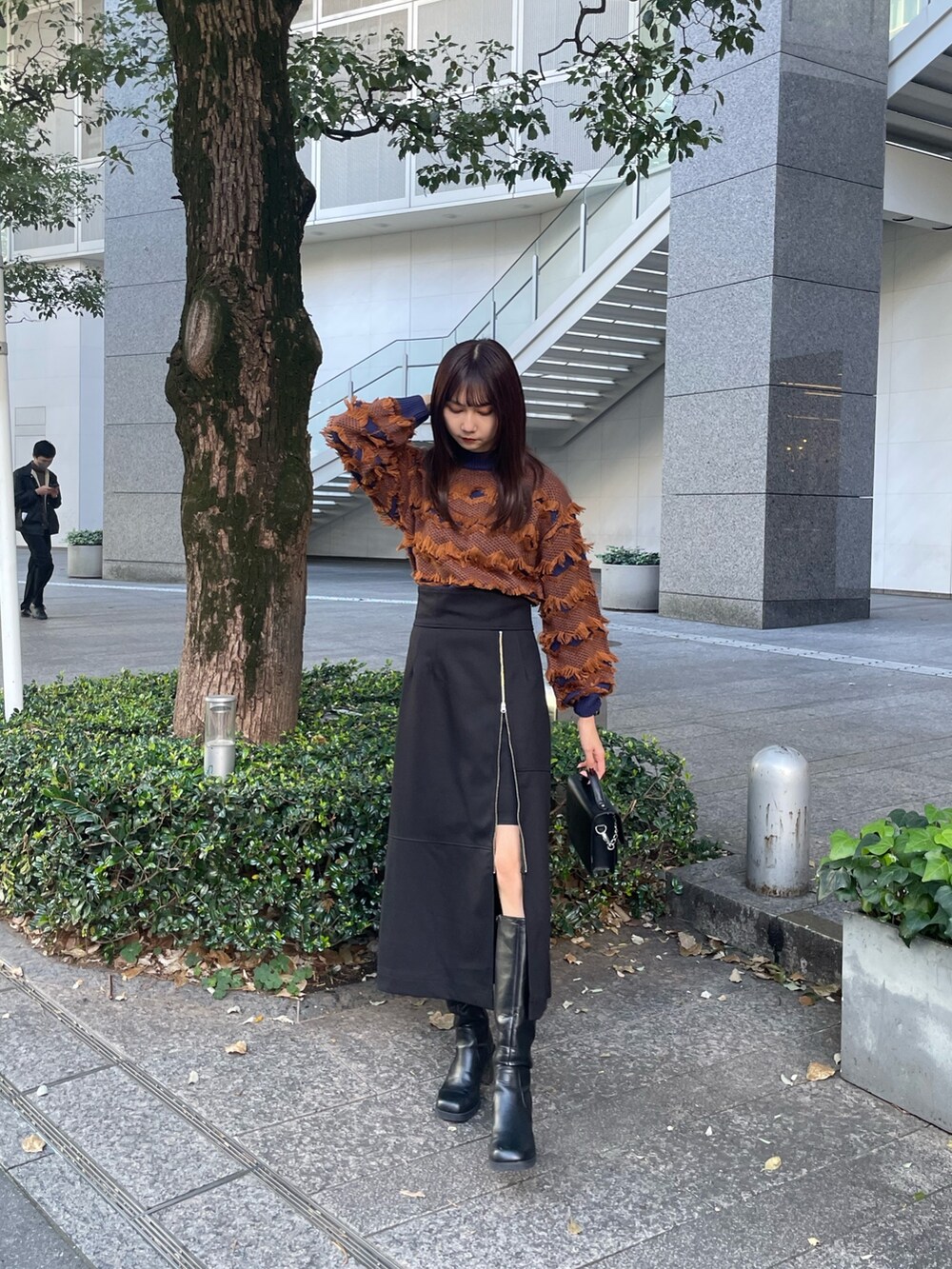 オレンジ系のニット/セーター、ブラック系のスカート、ブラック系のブーツを着用したレディースの秋コーディネートの2枚目の写真