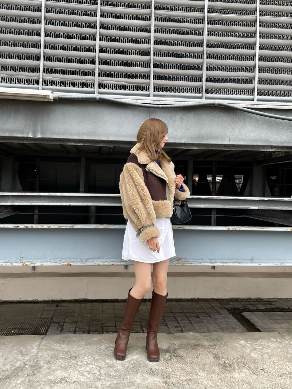 ブラウン系のムートンコート、ブラック系のハンドバッグ、ブラウン系のブーツを着用したレディースの秋コーディネートの2枚目の写真