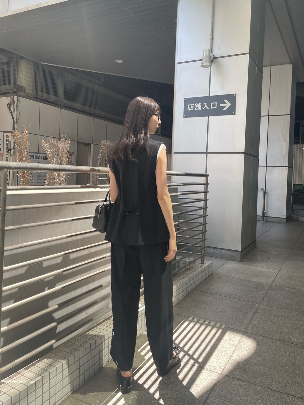 ブラック系のテーラードジャケット、ホワイト系のタンクトップ、ブラック系のスラックスを着用したレディースの春コーディネートの3枚目の写真