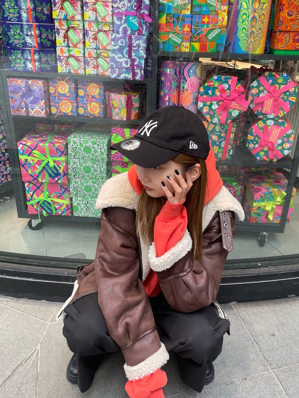 オレンジ系のパーカー、ブラウン系のムートンコート、ブラック系のスラックスを着用したレディースの秋コーディネートの4枚目の写真