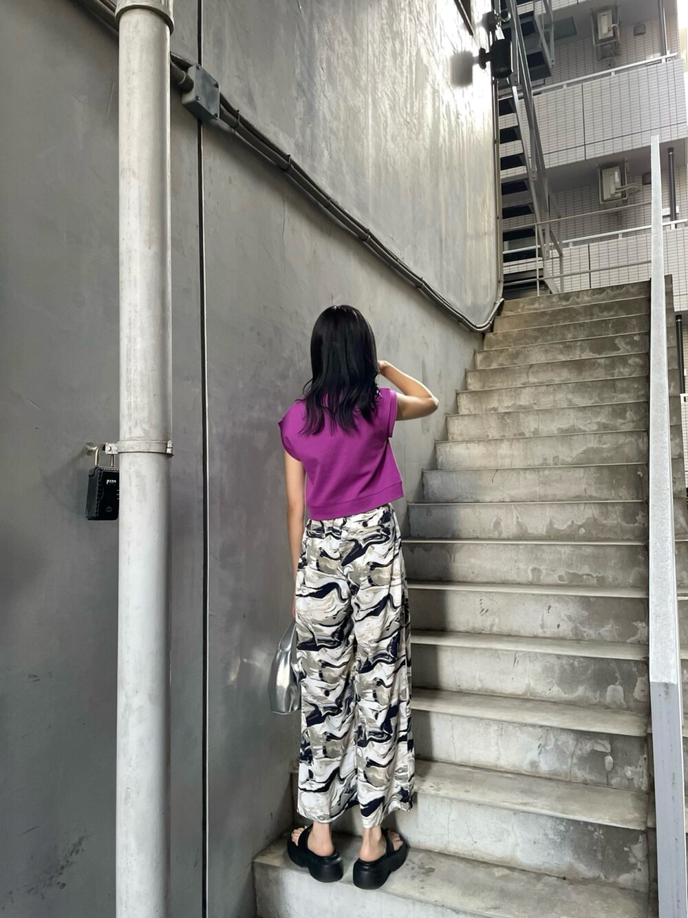 パープル系のタンクトップ、シルバー系のハンドバッグ、ブルー系のスラックスを着用したレディースの春コーディネートの3枚目の写真