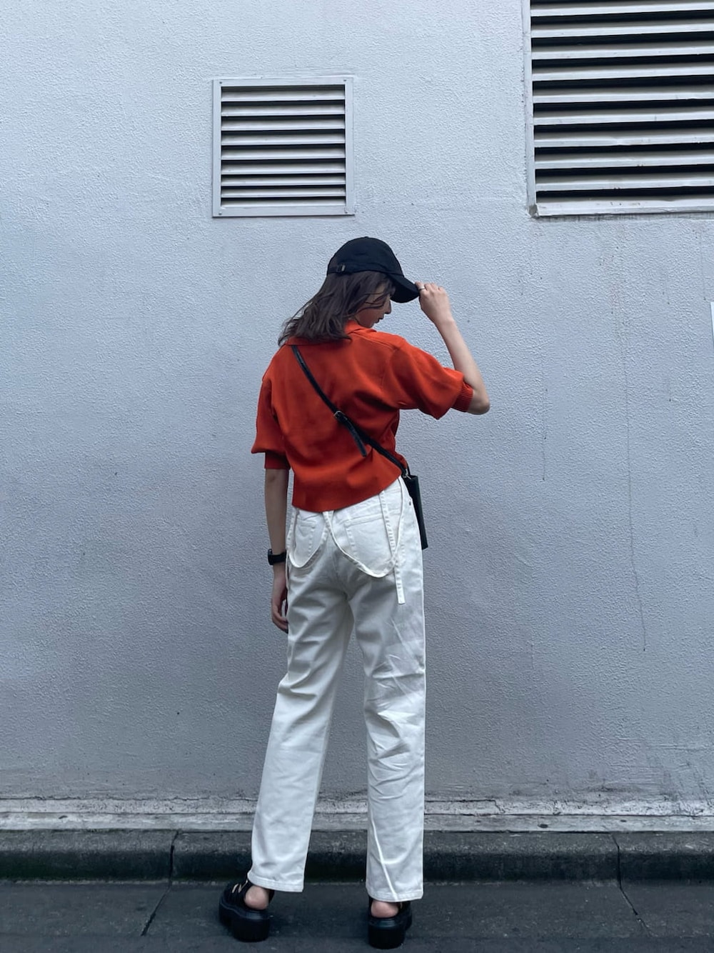 オレンジ系のポロシャツ、ホワイト系のデニムパンツ、ブラック系のサンダルを着用したレディースの夏コーディネートの3枚目の写真