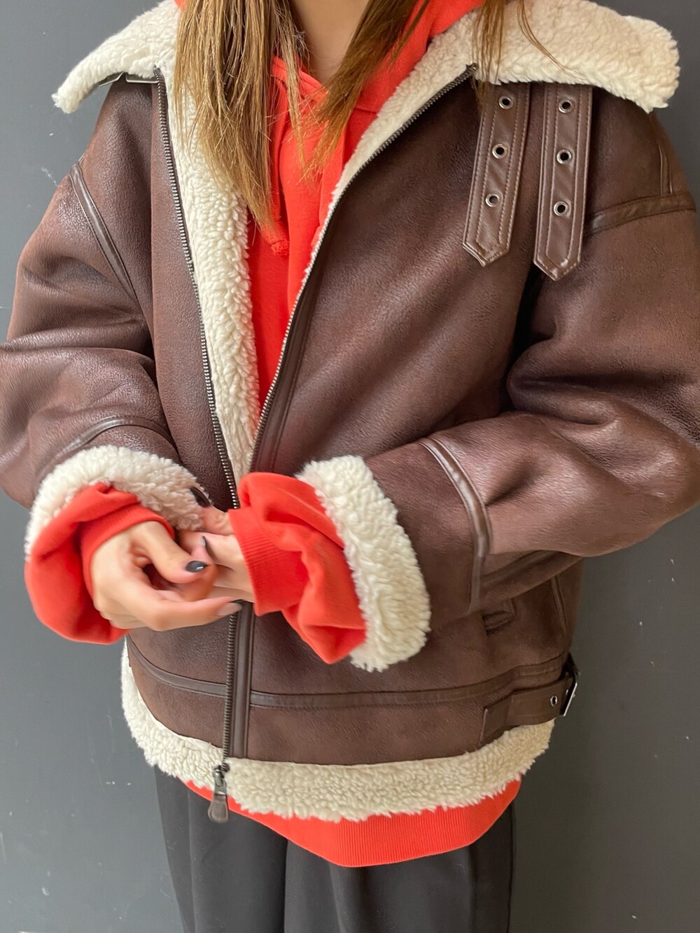 オレンジ系のパーカー、ブラウン系のムートンコート、ブラック系のスラックスを着用したレディースの秋コーディネートの6枚目の写真