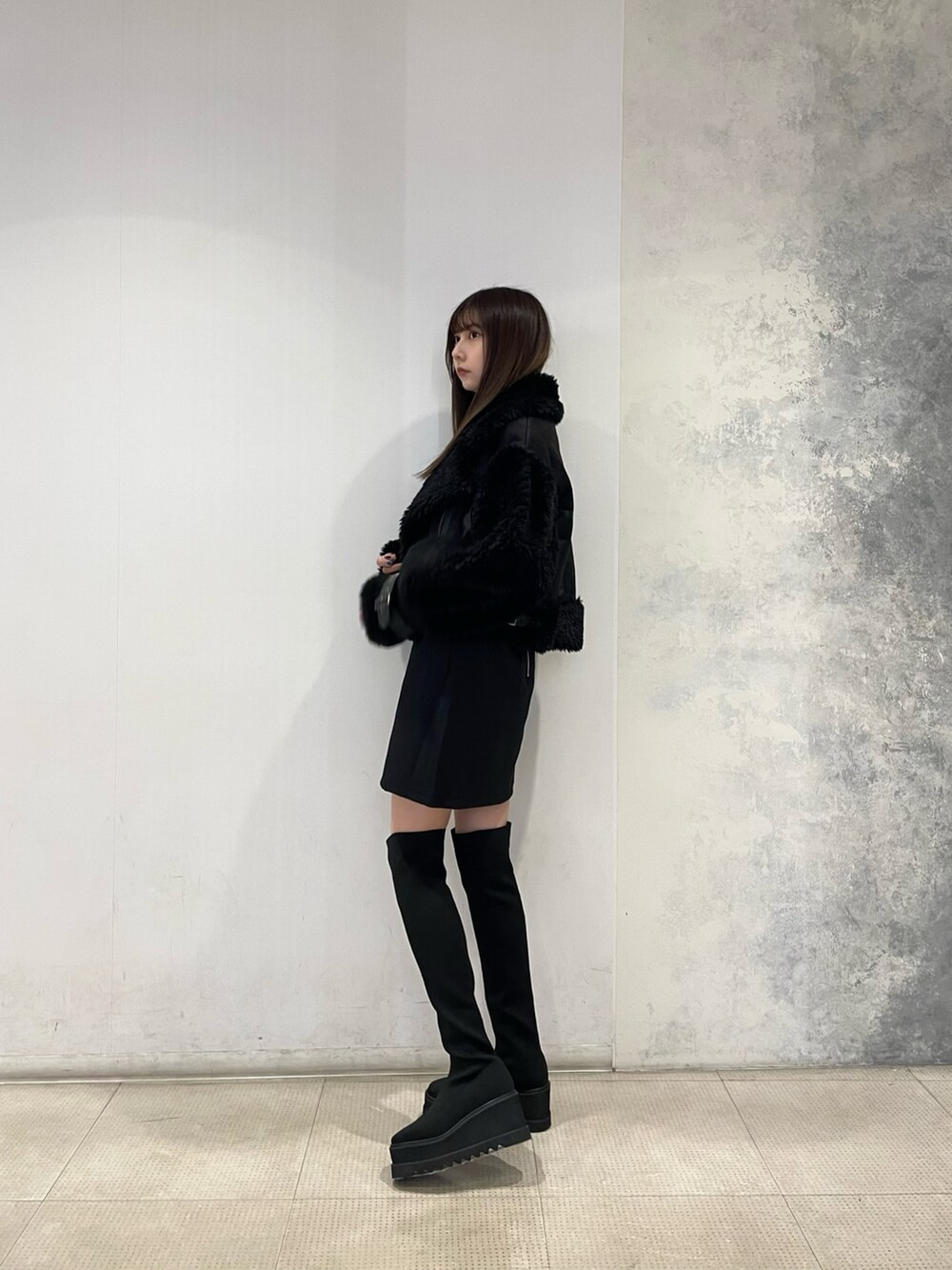 ブラック系のムートンコート、イエロー系のニット/セーター、ブラック系のスカートを着用したレディースの秋コーディネートの2枚目の写真