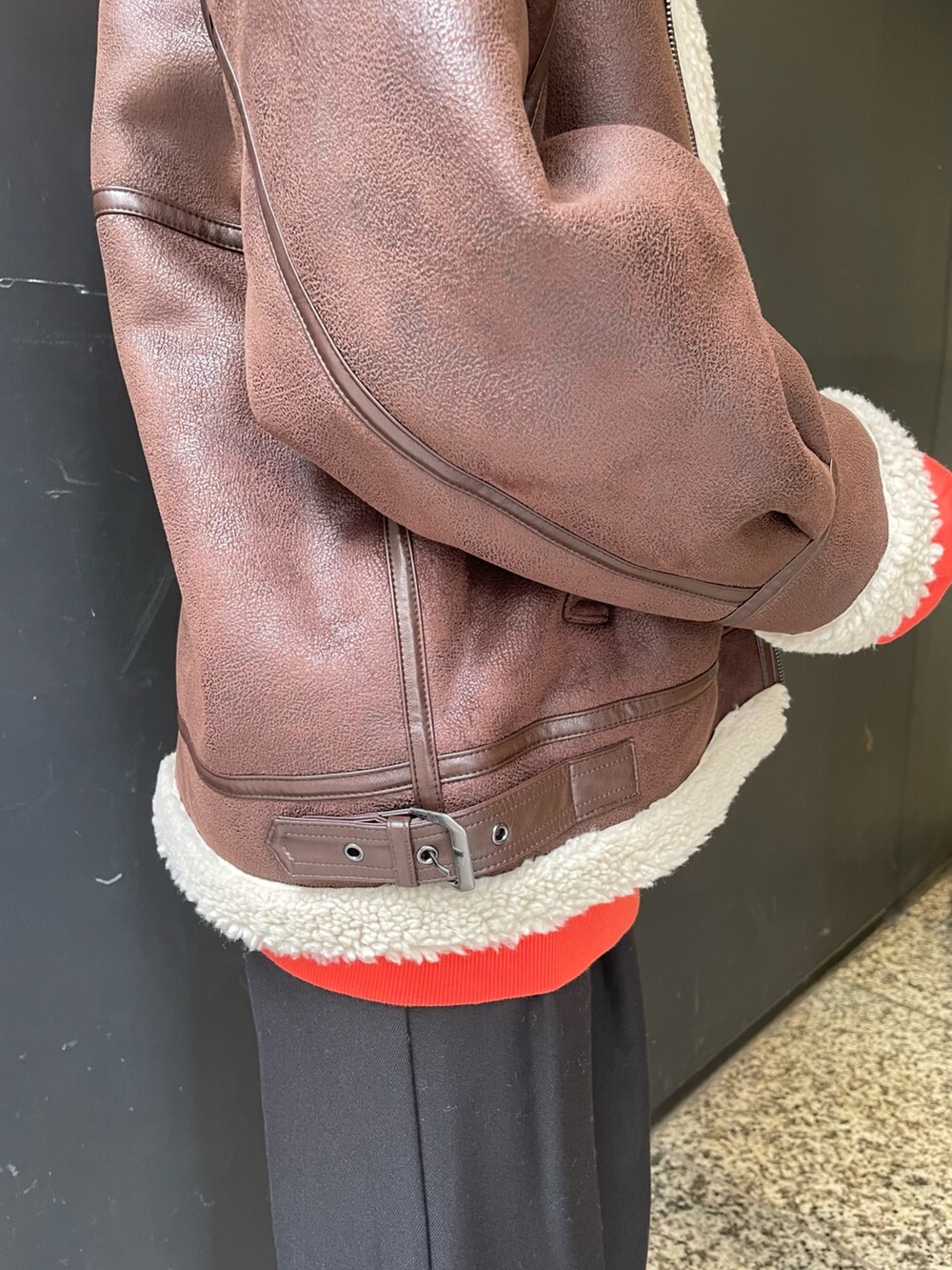 オレンジ系のパーカー、ブラウン系のムートンコート、ブラック系のスラックスを着用したレディースの秋コーディネートの7枚目の写真