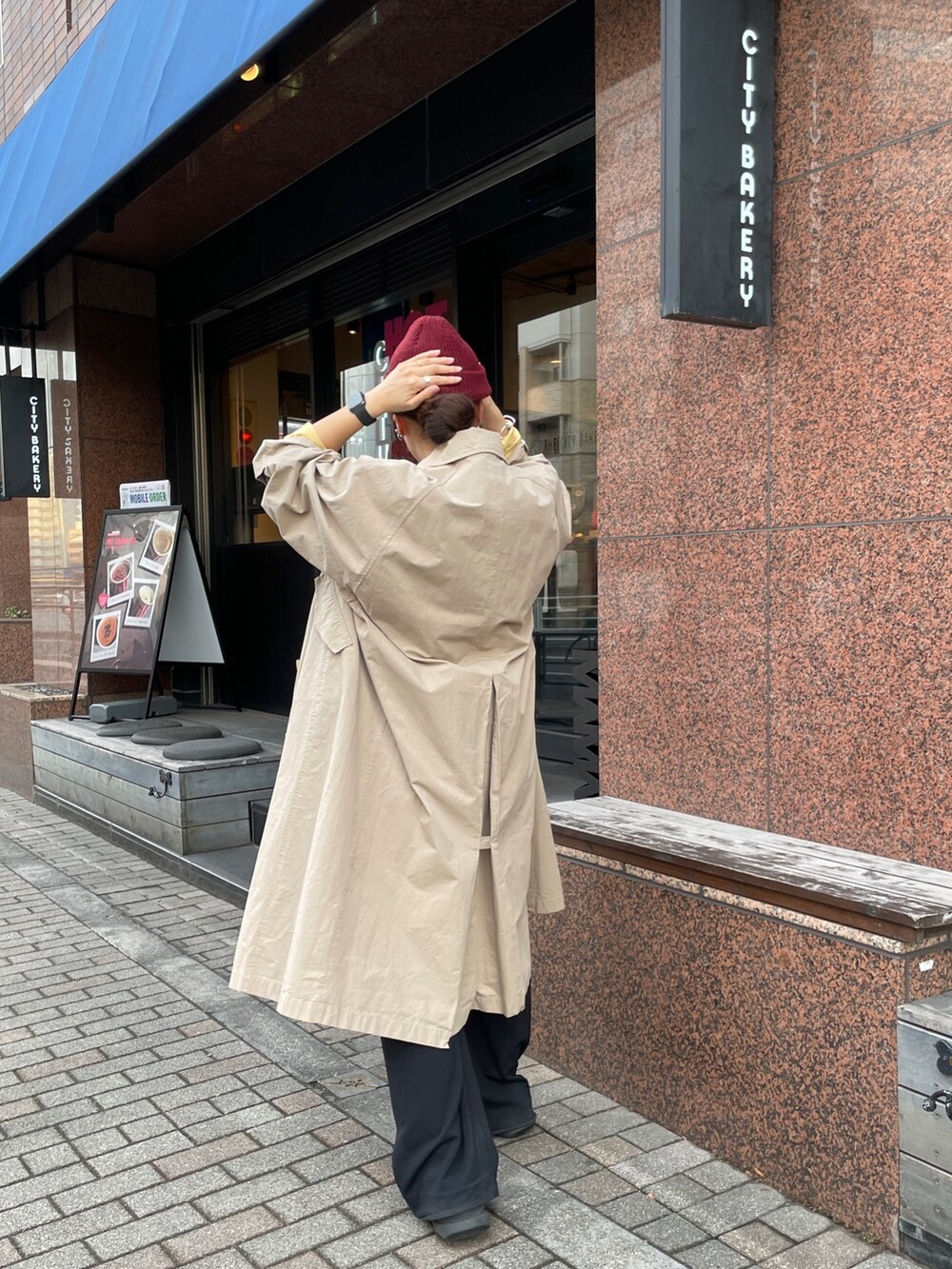 ベージュ系のステンカラーコート、イエロー系のTシャツ/カットソーを着用したレディースの冬コーディネートの3枚目の写真