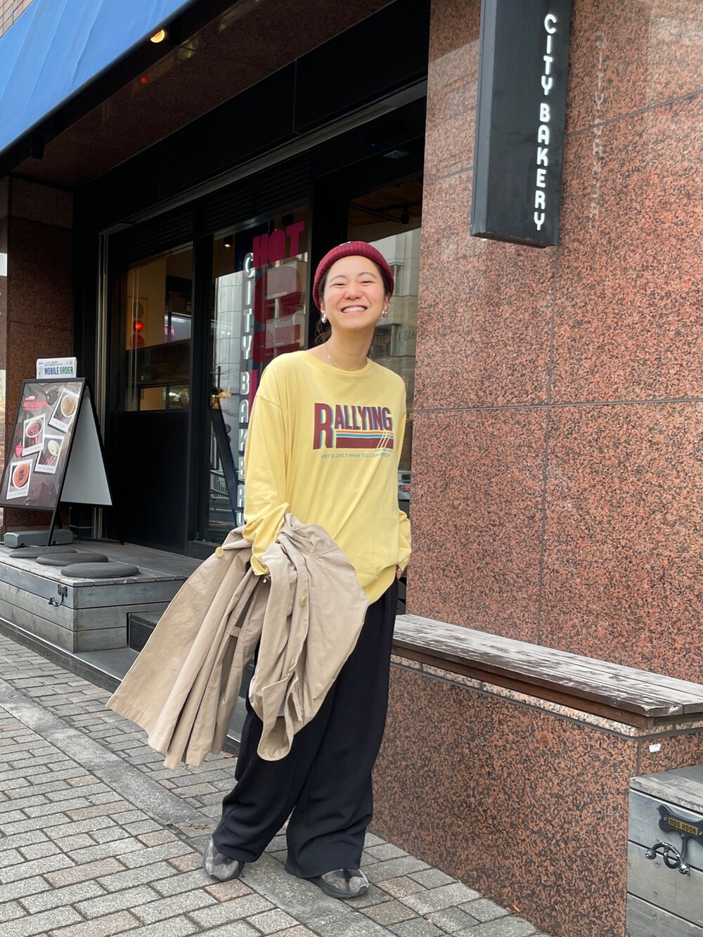 ベージュ系のステンカラーコート、イエロー系のTシャツ/カットソーを着用したレディースの冬コーディネートの4枚目の写真