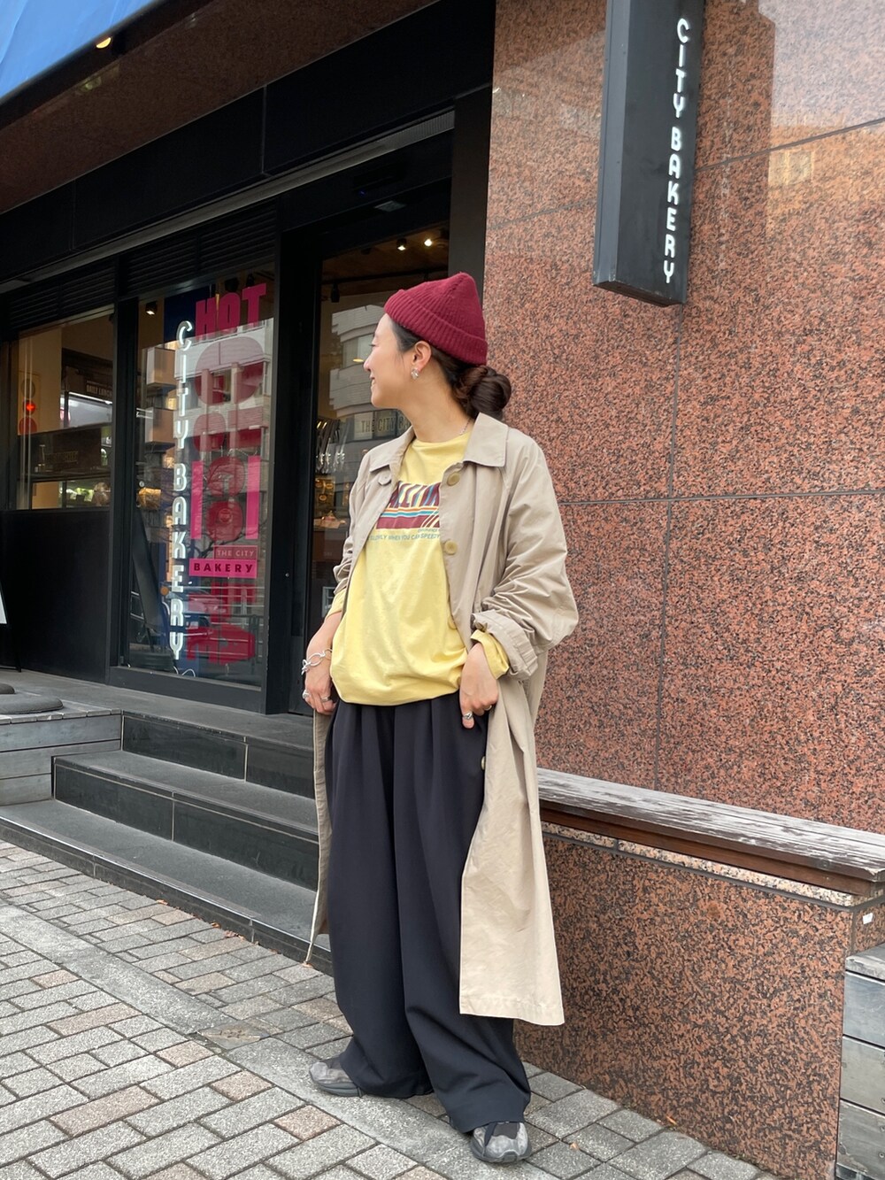 ベージュ系のステンカラーコート、イエロー系のTシャツ/カットソーを着用したレディースの冬コーディネートの2枚目の写真