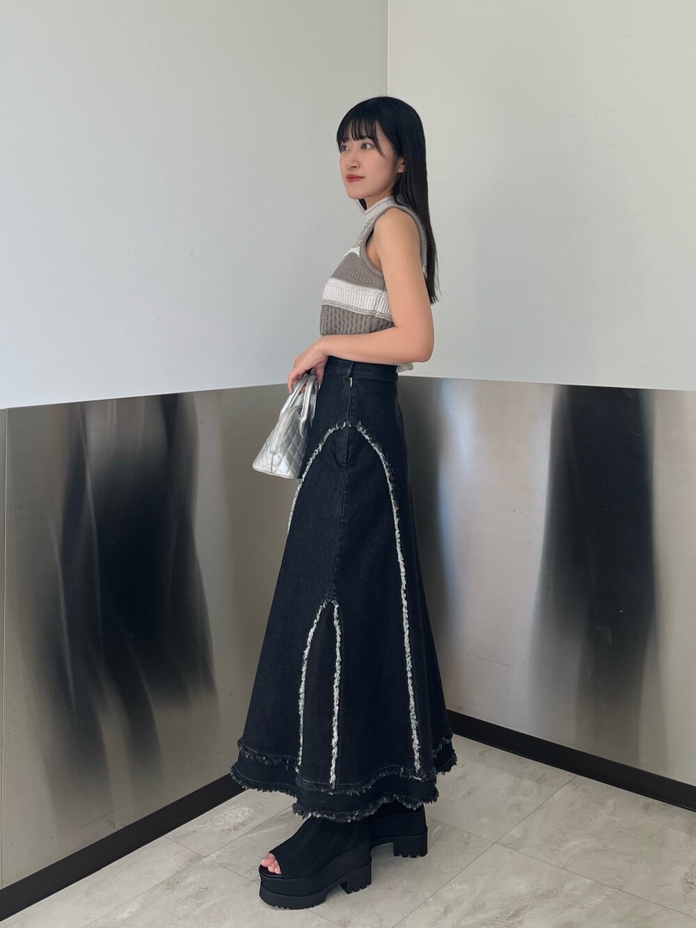 グレー系のニット/セーター、ブラック系のデニムスカート、ブラック系のブーツを着用したレディースの春コーディネートの3枚目の写真