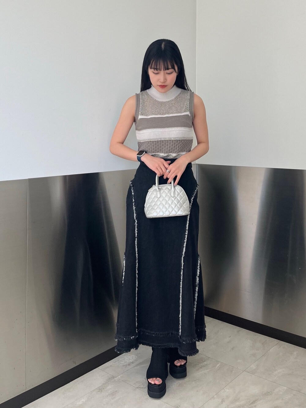 グレー系のニット/セーター、ブラック系のデニムスカート、ブラック系のブーツを着用したレディースの春コーディネートの2枚目の写真