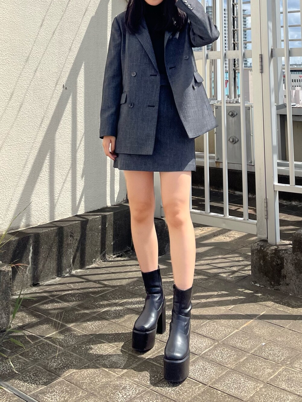 グレー系のテーラードジャケット、グレー系のスカート、ブラック系のブーツを着用したレディースの秋コーディネートの2枚目の写真