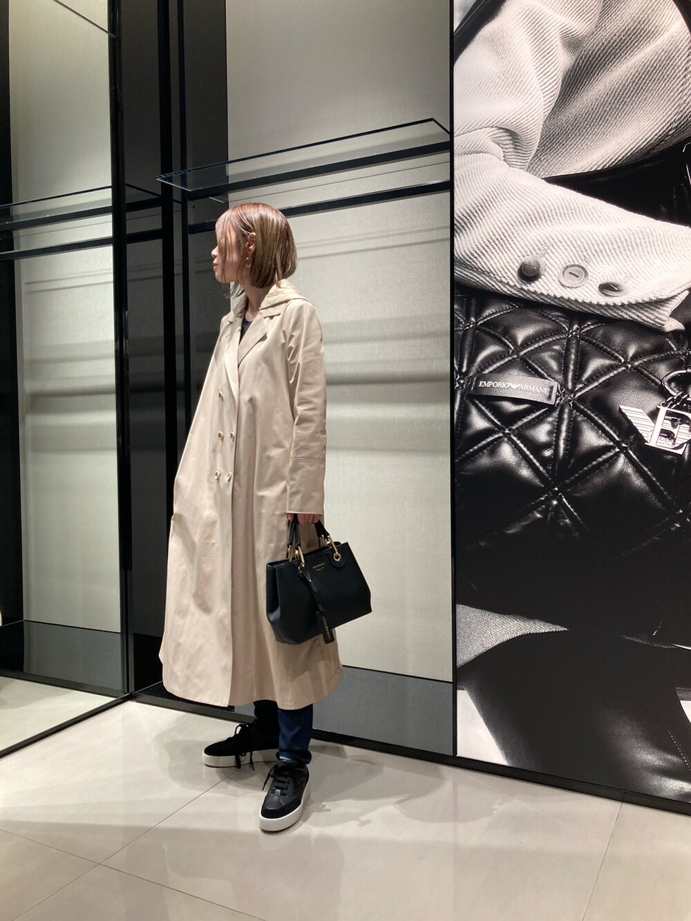 ベージュ系のトレンチコート、ブラック系のハンドバッグ、ブルー系のデニムパンツを着用したレディースの秋コーディネートの2枚目の写真