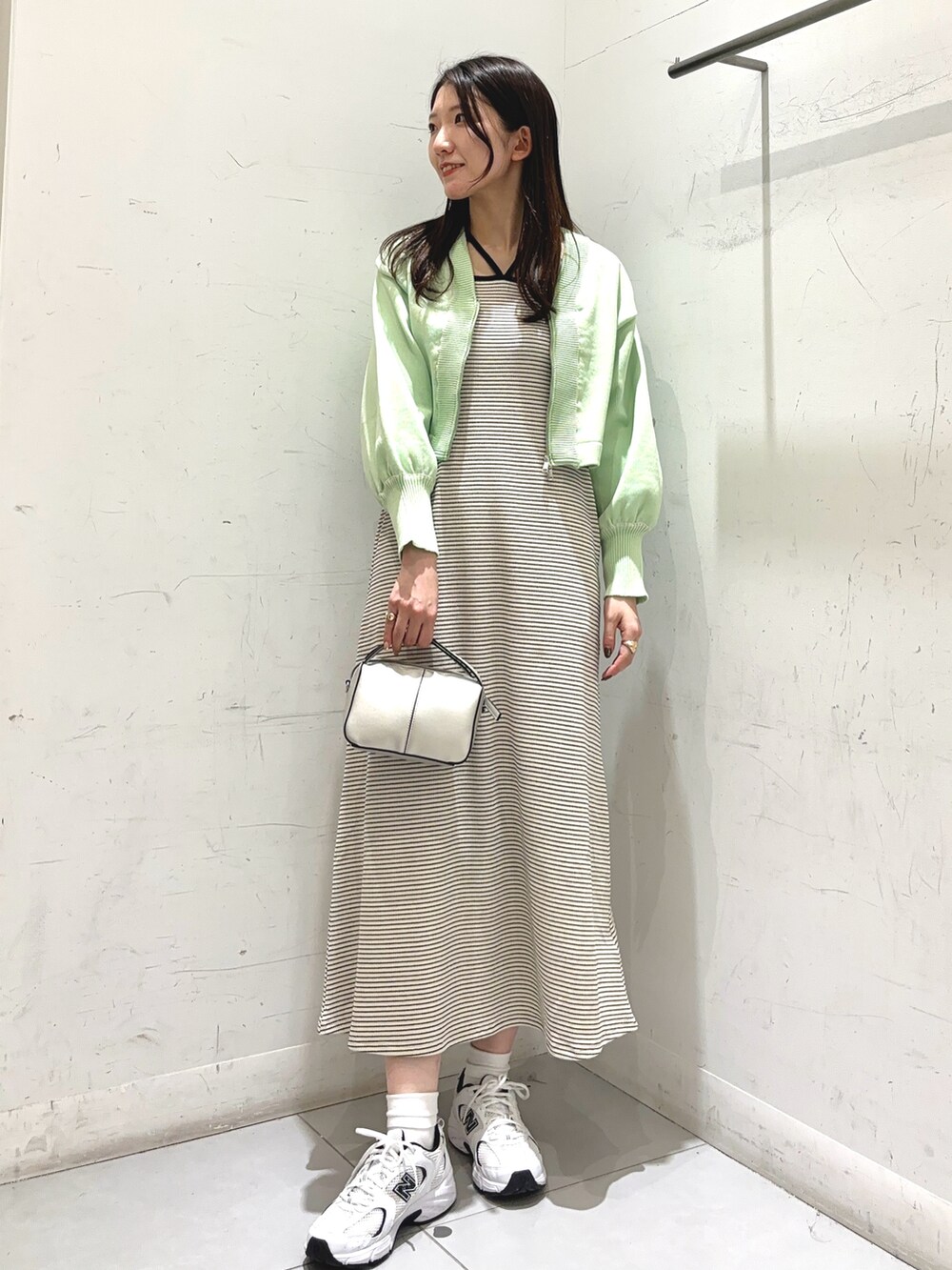 グリーン系のワンピース、ゴールド系のショルダーバッグ、ホワイト系のスニーカーを着用したレディースの冬コーディネートの2枚目の写真