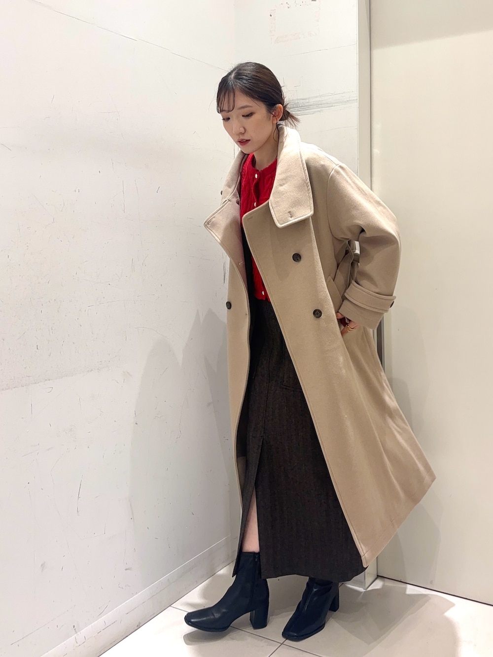 レッド系のカーディガン/ボレロ、ベージュ系のステンカラーコート、ブラウン系のスカートを着用したレディースの秋コーディネートの3枚目の写真
