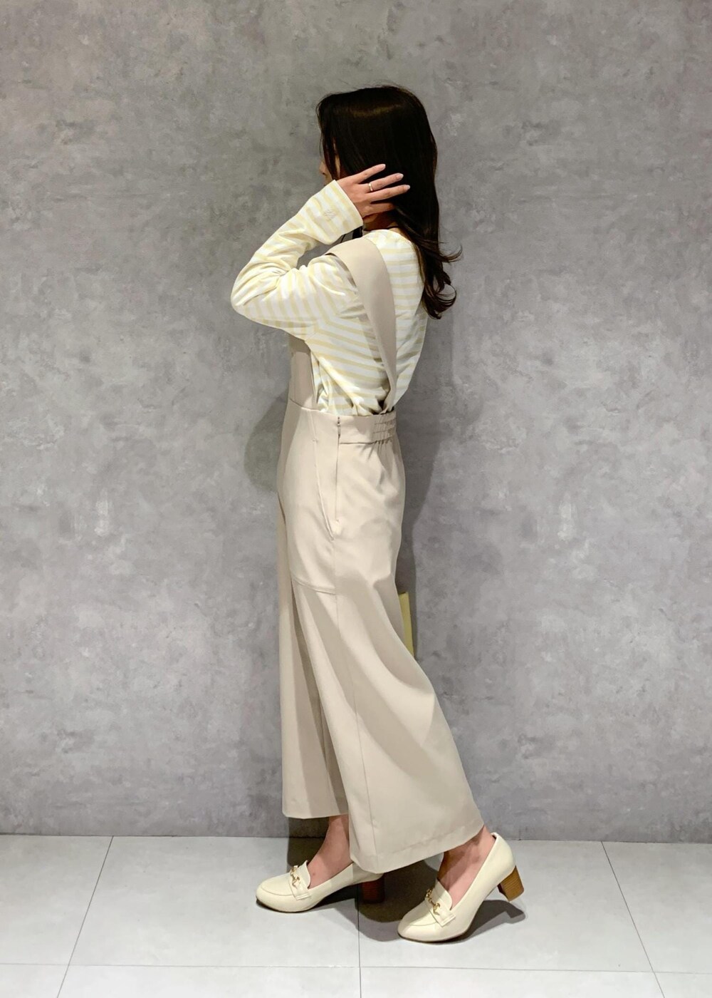 イエロー系のトートバッグ、ベージュ系のジャンパースカート、ベージュ系のTシャツ/カットソーを着用したレディースの冬コーディネートの4枚目の写真